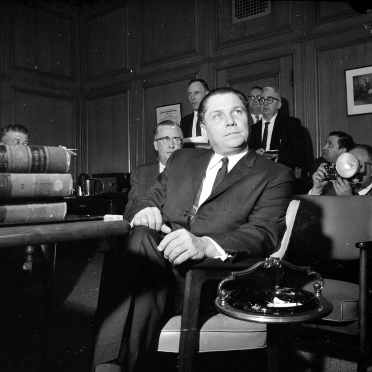 Portrait of Teamster Union leader, Jimmy Hoffa sitting in chair with unidentified men in background during newspaper strike of 1962 in Detroit, Michigan.