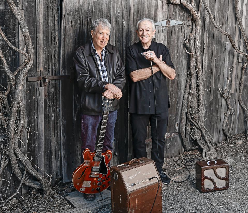 Elvin Bishop and Charlie Musselwhite in rehearsal, standing against an old fence